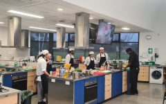 Group of students standing in a kitchen together and learning from the master chef
